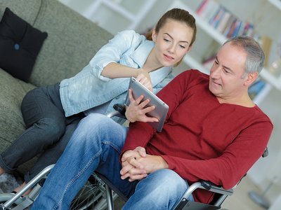 Junge Frau zeigt Mann im Rollstuhl etwas auf dem Tablet Beratung-allgemein.jpg
