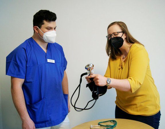Praxisanleiterin zeigt Schüler das Blutdruckmessen